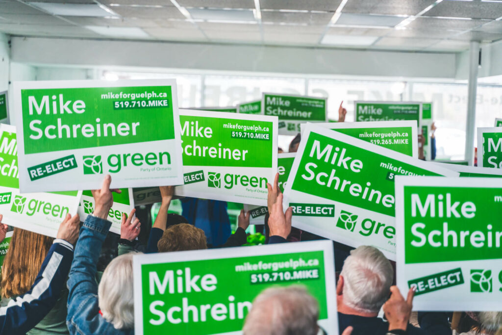 A group of people holding Mike Schreiner signs, celebrating.